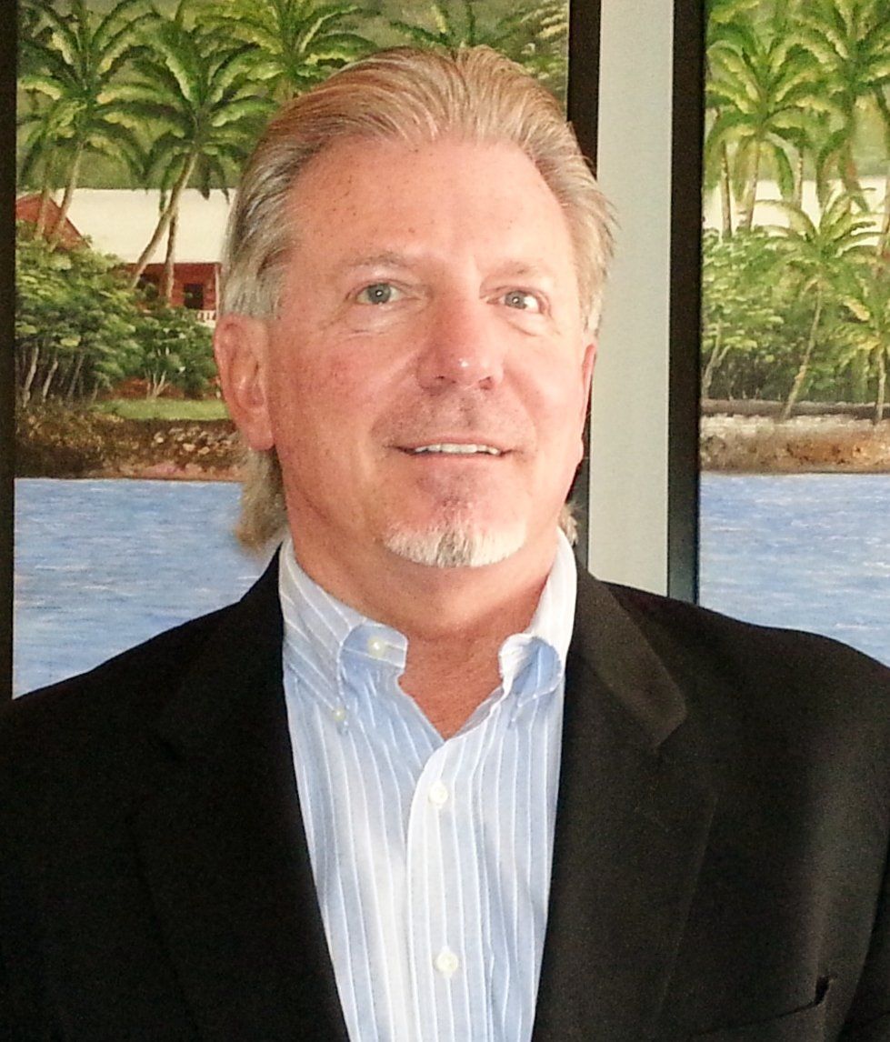 Man in blazer and open-collar shirt smiles; backdrop depicts tropical landscape.