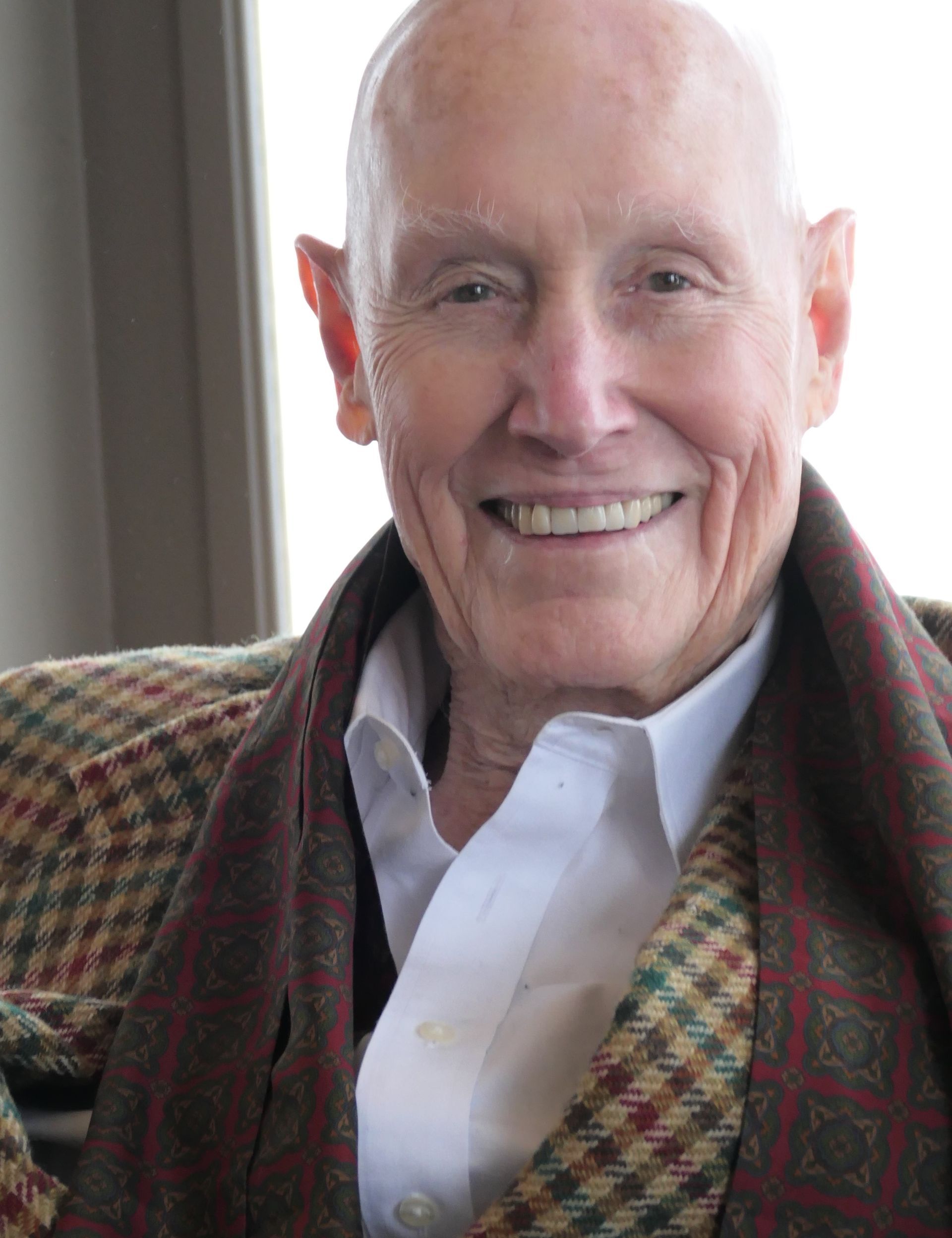Smiling older man in tweed jacket and white shirt.