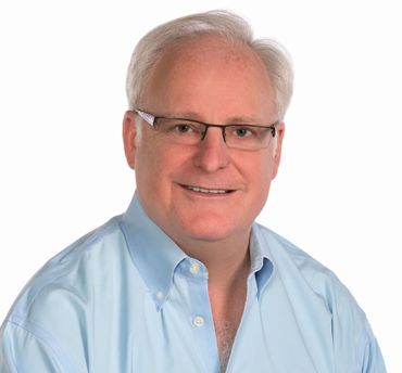 Man in blue shirt, glasses, smiles at camera.