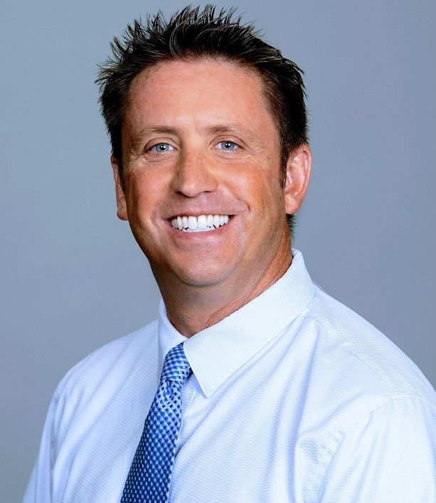 Man smiling in a light blue shirt and patterned tie.