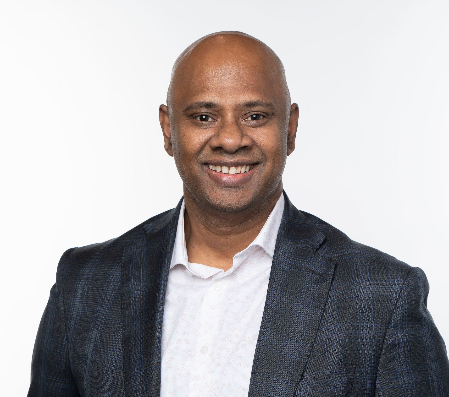 Bald man in a dark blazer smiling, set against a white background.