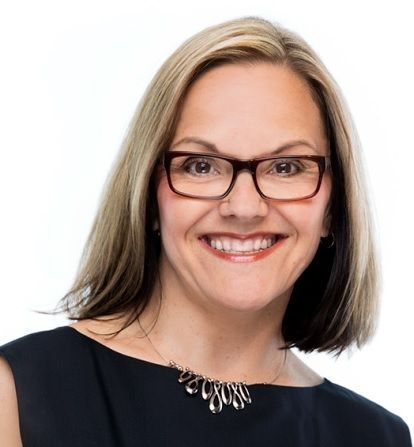 Woman wearing glasses smiles at the camera, wearing a black top and silver necklace.