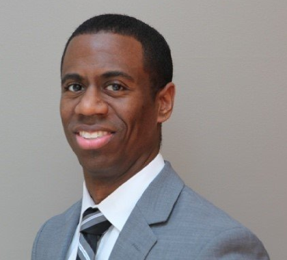 Man in gray suit and tie smiles, looking toward the camera.