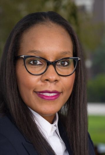 Woman wearing glasses and a dark blazer, smiling, outdoors.