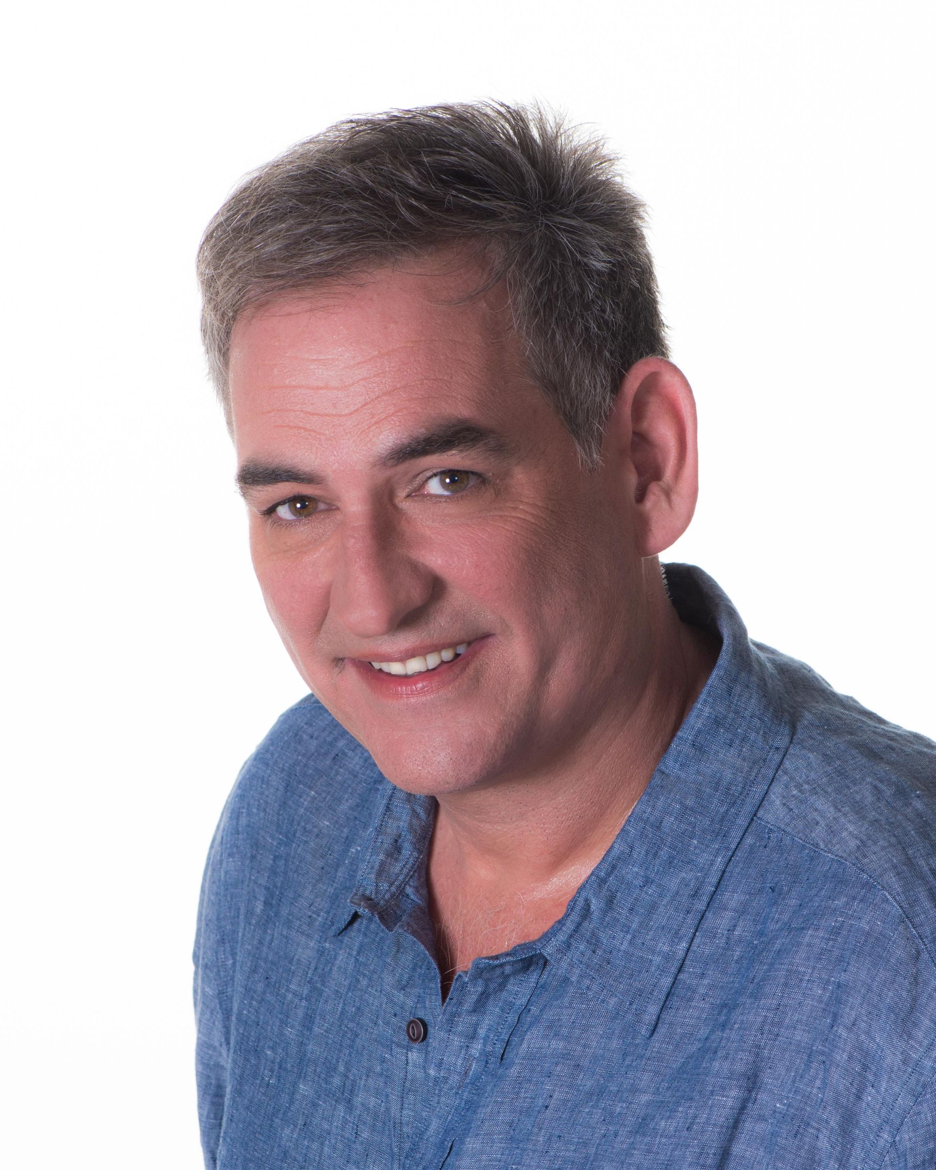 Man smiling, wearing a blue shirt, against a white backdrop.