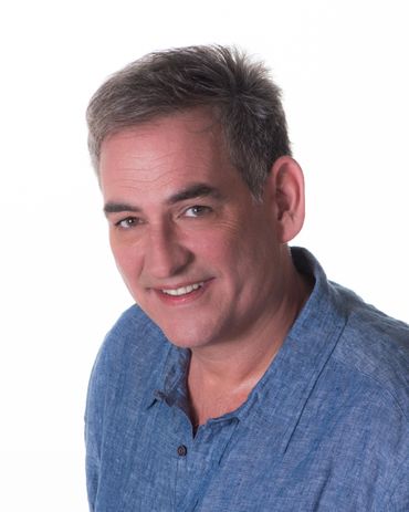Man smiling, wearing a blue shirt, against a white backdrop.