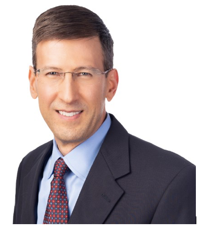 Man in glasses, smiling, wearing a suit and tie.