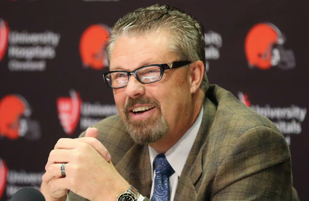 Man in glasses, brown jacket, speaking at a press conference with Browns logo in background.