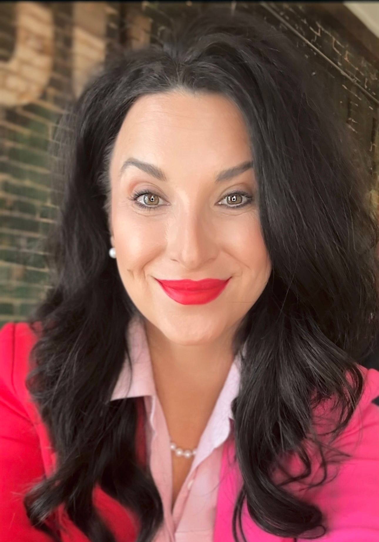 Woman with dark hair smiles, wearing a pink shirt and a red jacket.