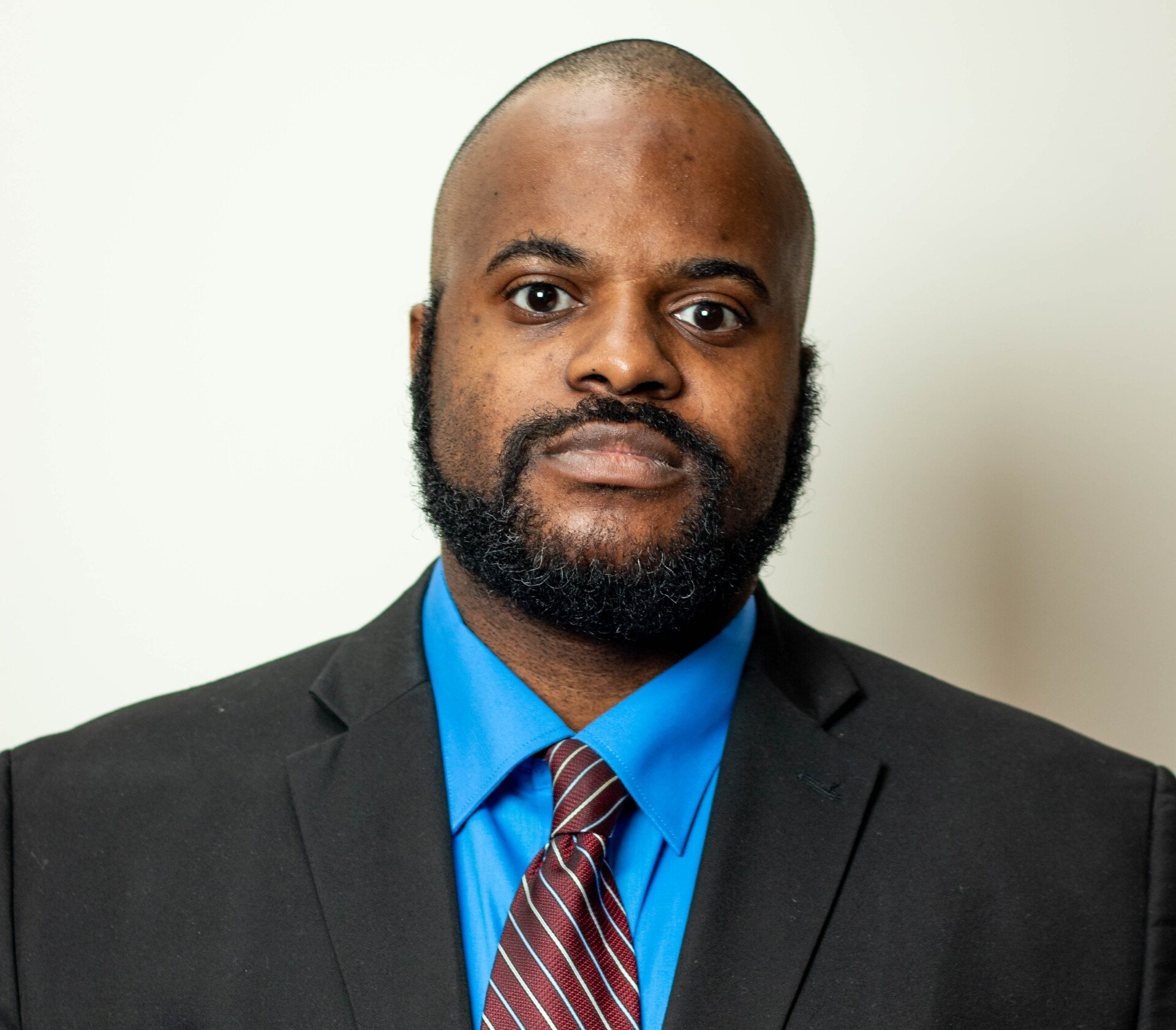 Man wearing a suit and tie, against a white background.