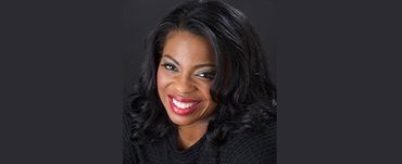 Woman with dark hair smiles, wearing dark clothing against a dark background.