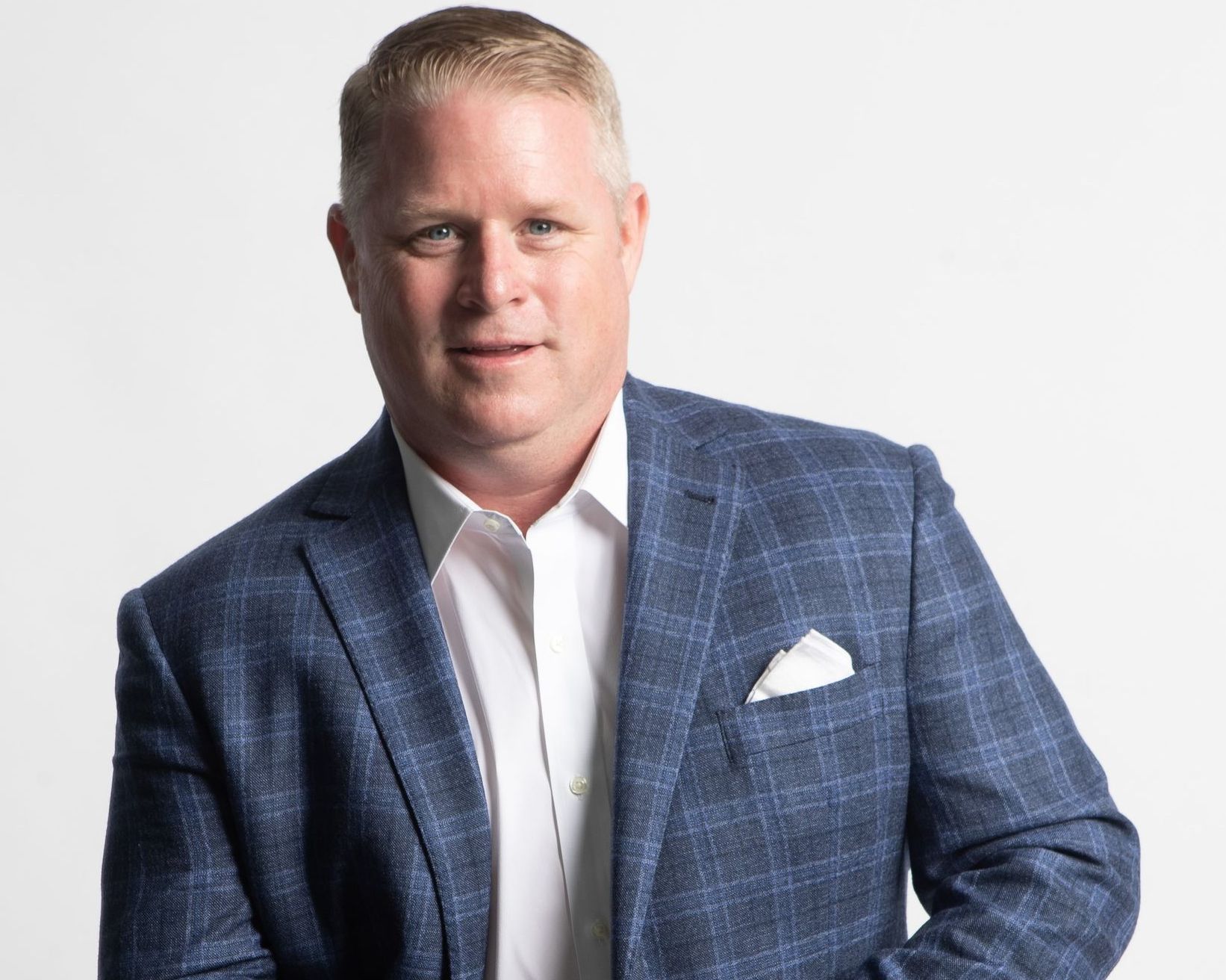 Man in blue plaid blazer and white shirt, smiling, looking at the camera.