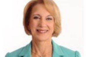 Woman in a turquoise blazer smiles, posing in front of a white background.