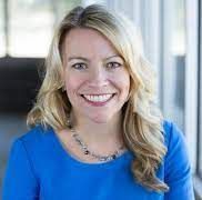Woman with blonde hair wearing a blue shirt smiles.