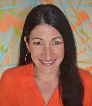 Woman with dark hair smiles, wearing an orange shirt and gold hoop earrings. Background: colorful abstract art.