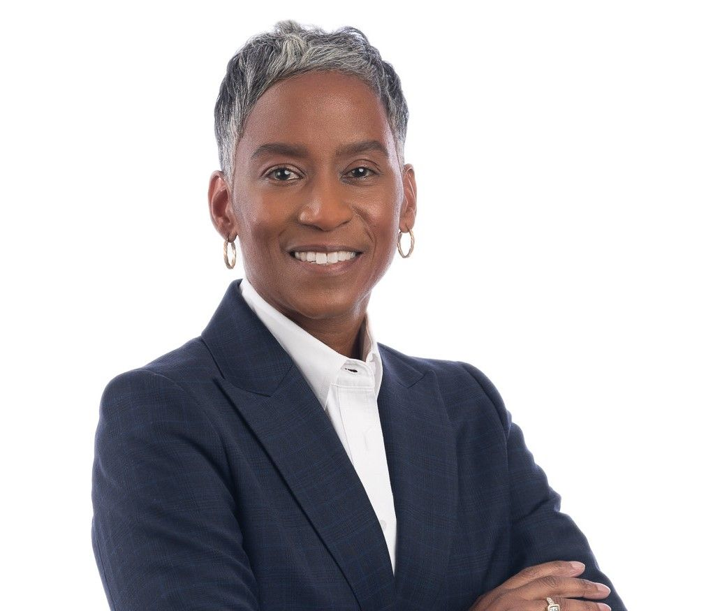 Smiling person in a dark suit, arms crossed, white background.
