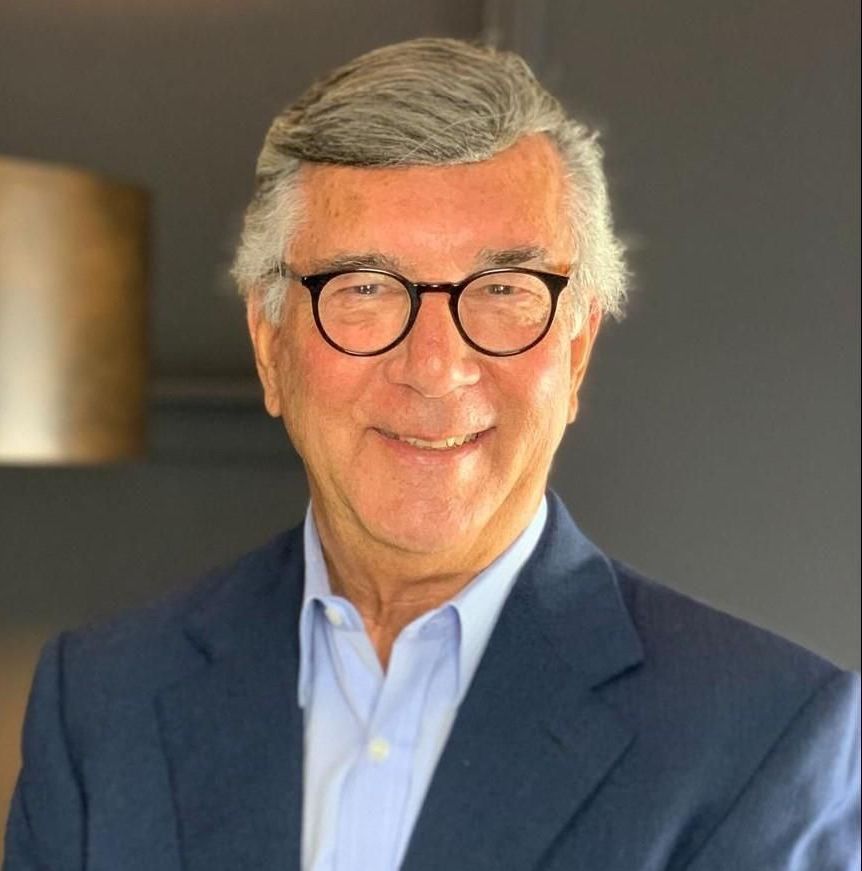 Man in glasses, blue blazer and light blue shirt smiles.