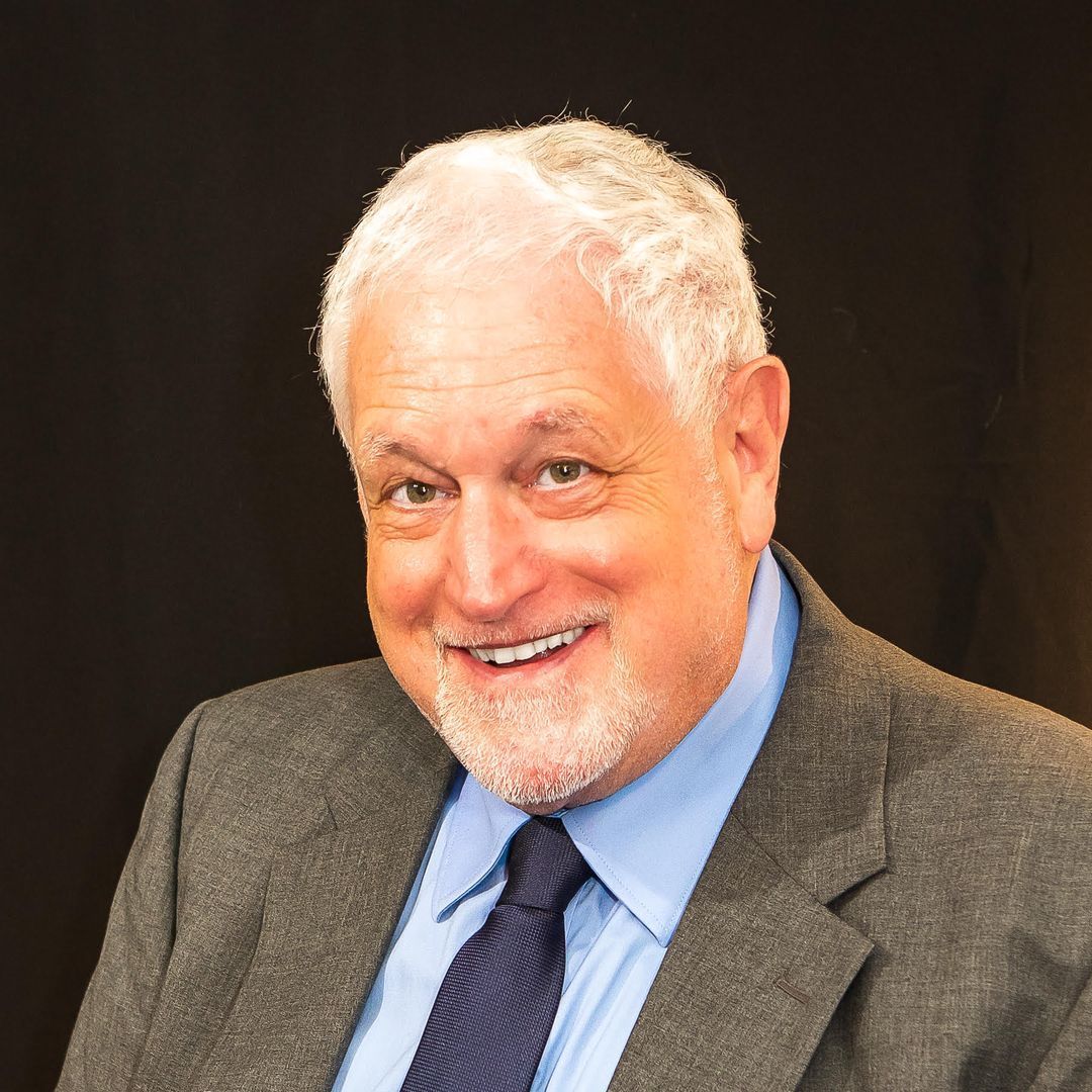 Man in gray suit smiles, looking at the camera.