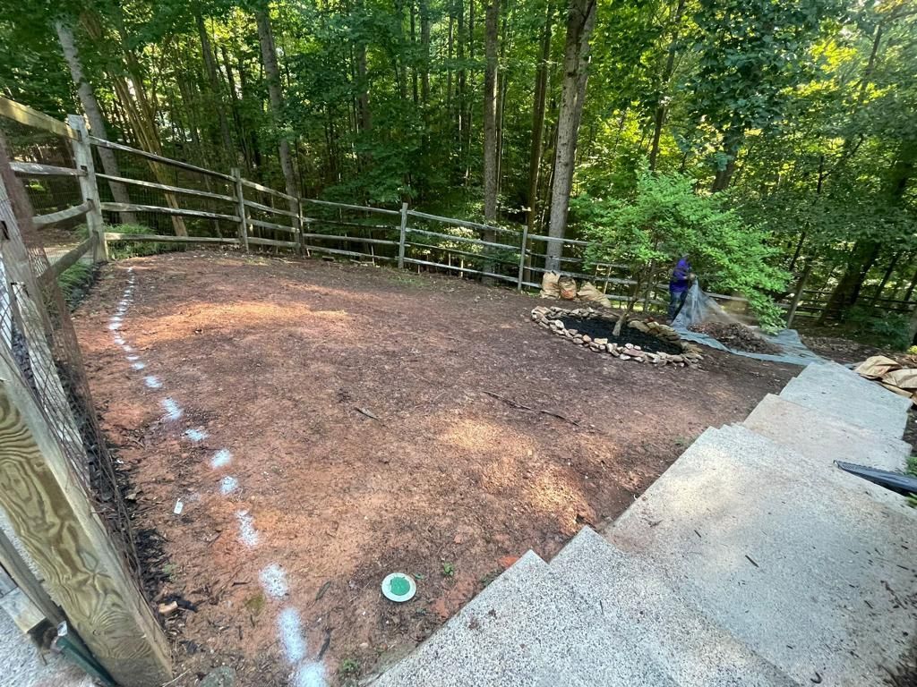A mulched backyard with a split-rail fence, stairs, and a person tending a small tree.