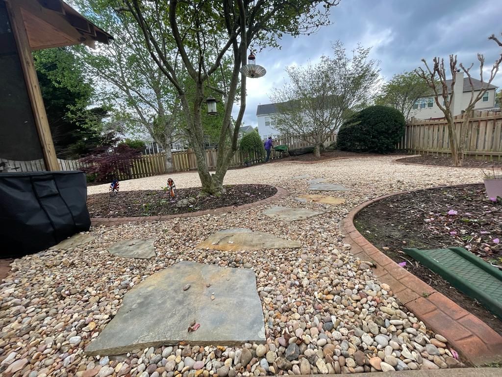 Stone path through a gravel yard with a tree in the center and a wooden fence in the background.
