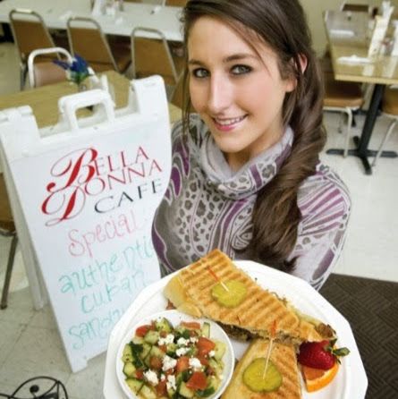 Woman holding a tray of food and a café sign at Bella Nina Café