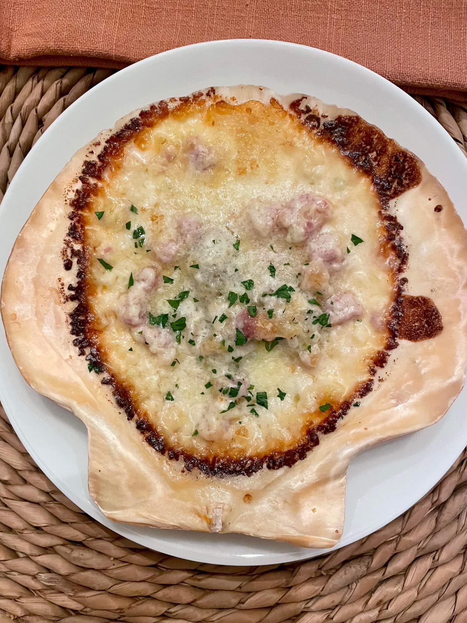 Baked cheesy dish in a shell-shaped crust on a white plate, topped with herbs.