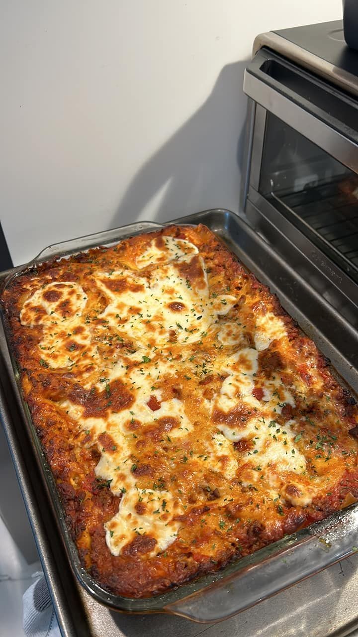 Baked lasagna in a glass dish, browned and bubbling on a countertop next to an oven.