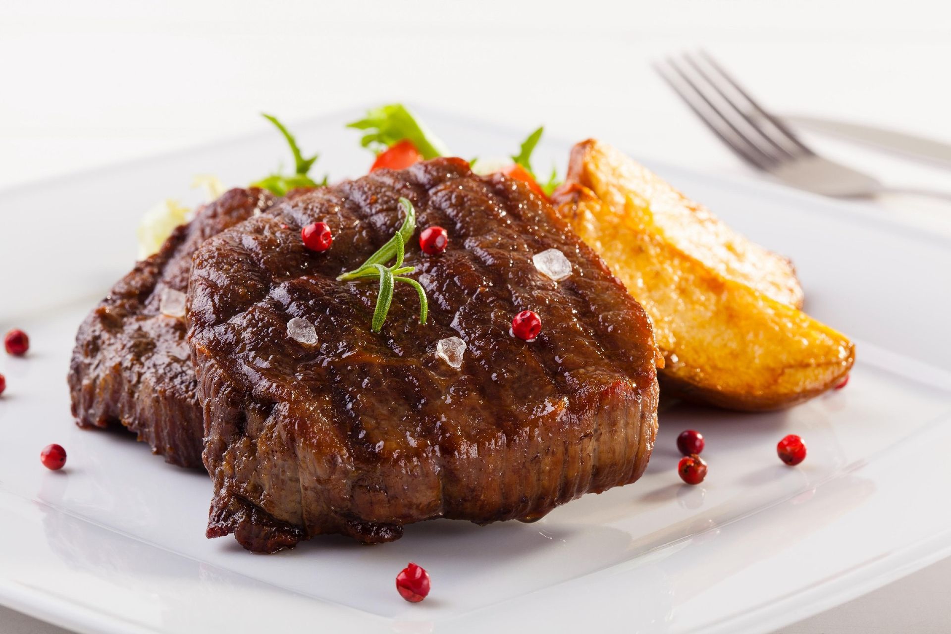 Seared steak with potatoes and red peppercorns on a white plate