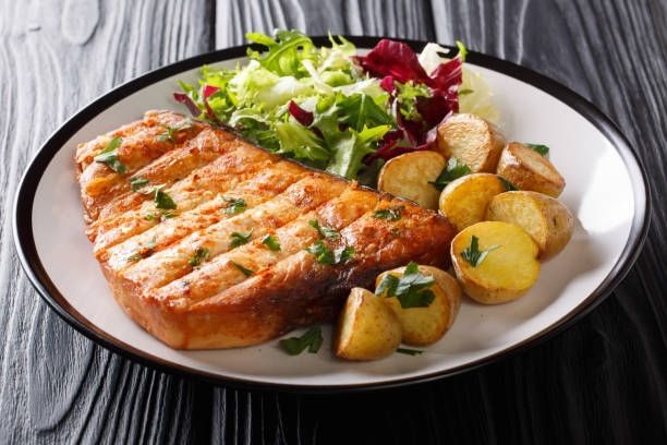Grilled salmon with salad and roasted potatoes on a white plate