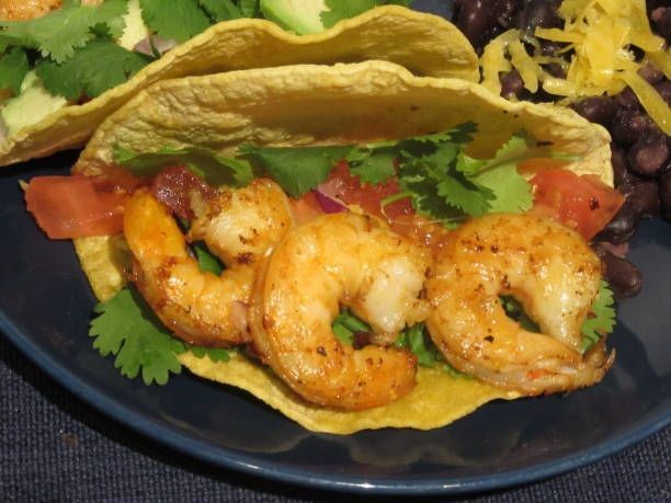 Shrimp tacos on corn tortillas with cilantro, tomato, and shredded cheese on a black plate