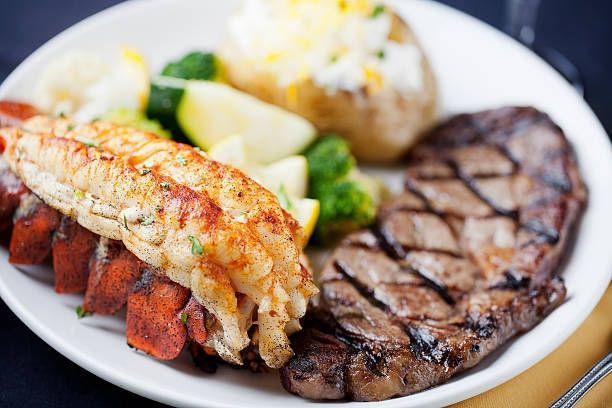 Grilled seafood and steak on a white plate with vegetables and mashed potatoes