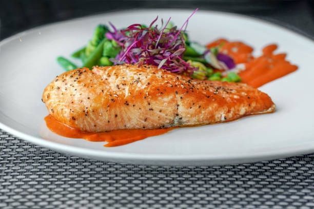 Grilled salmon fillet with roasted carrots, greens, and purple garnish on a white plate