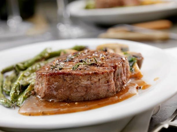 Seared steak with green asparagus on a white plate, drizzled with sauce, in a restaurant setting