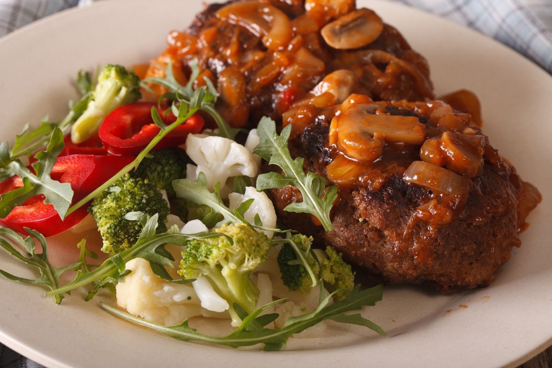 Plated steak topped with mushroom sauce beside mixed greens and sliced tomatoes