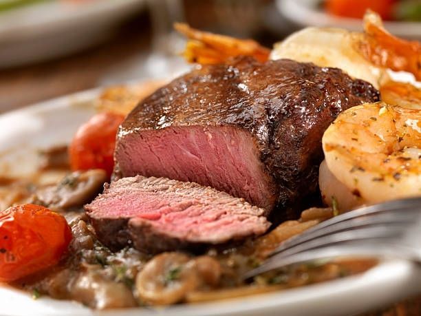 Plated medium-rare steak with roasted vegetables and fork on a white plate
