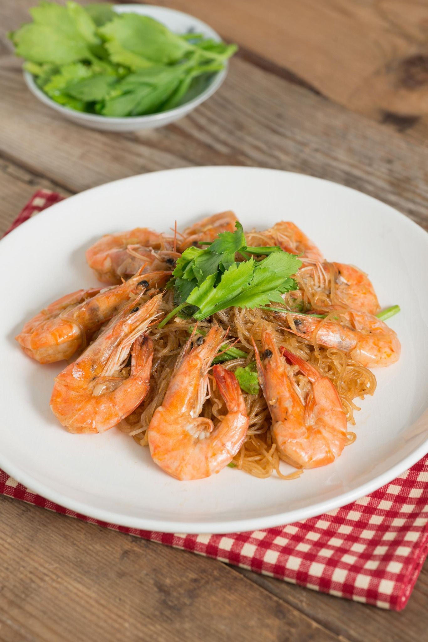 Plate of cooked shrimp garnished with herbs on a rustic table, with a bowl of lettuce in the background