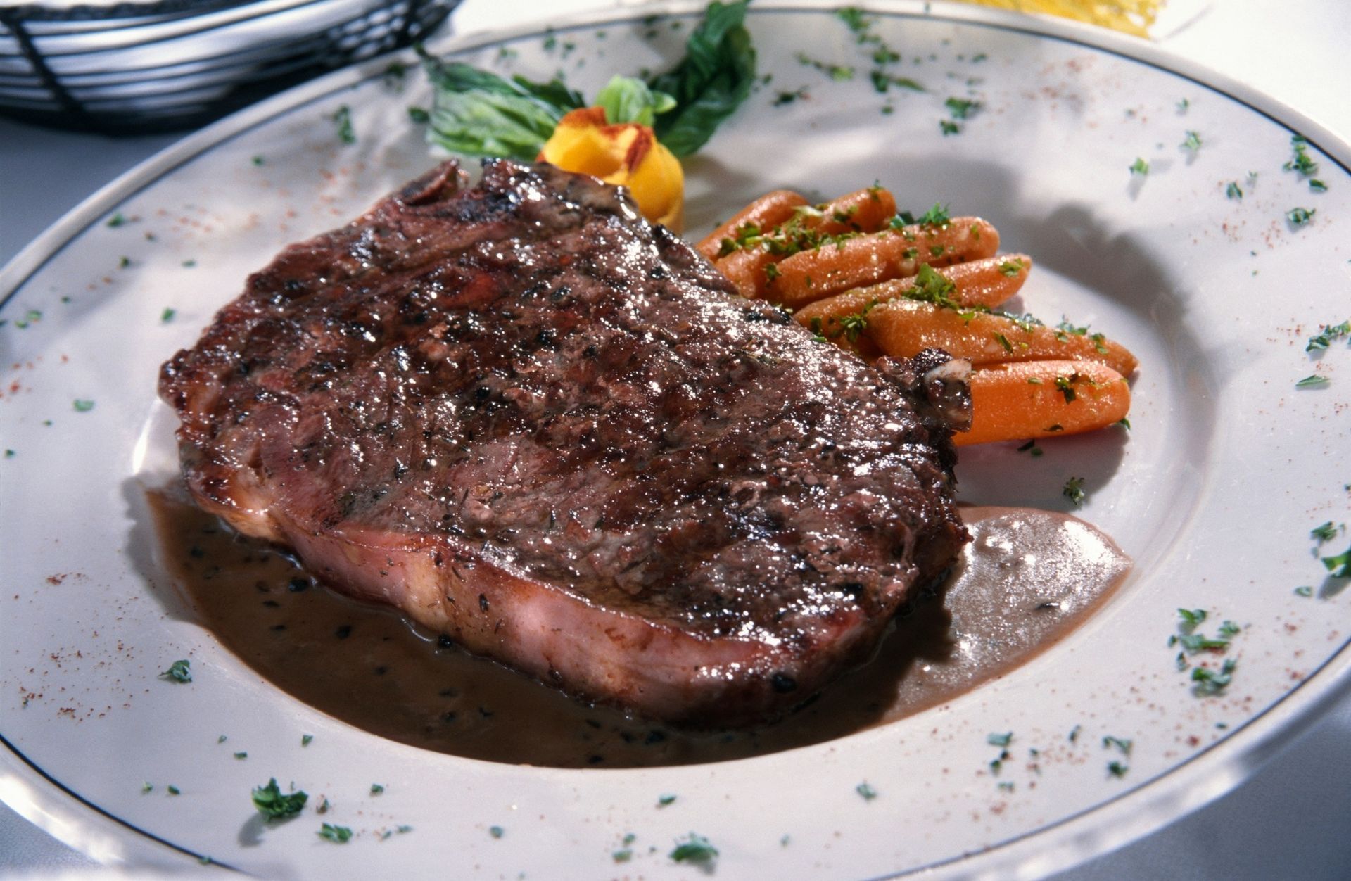 Grilled steak with sauce on a white plate, served with carrots and greens