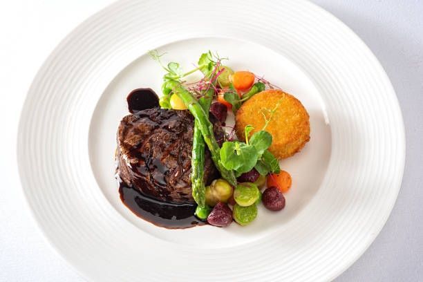 Plated gourmet steak with dark sauce, vegetables, and a round orange puree on a white plate