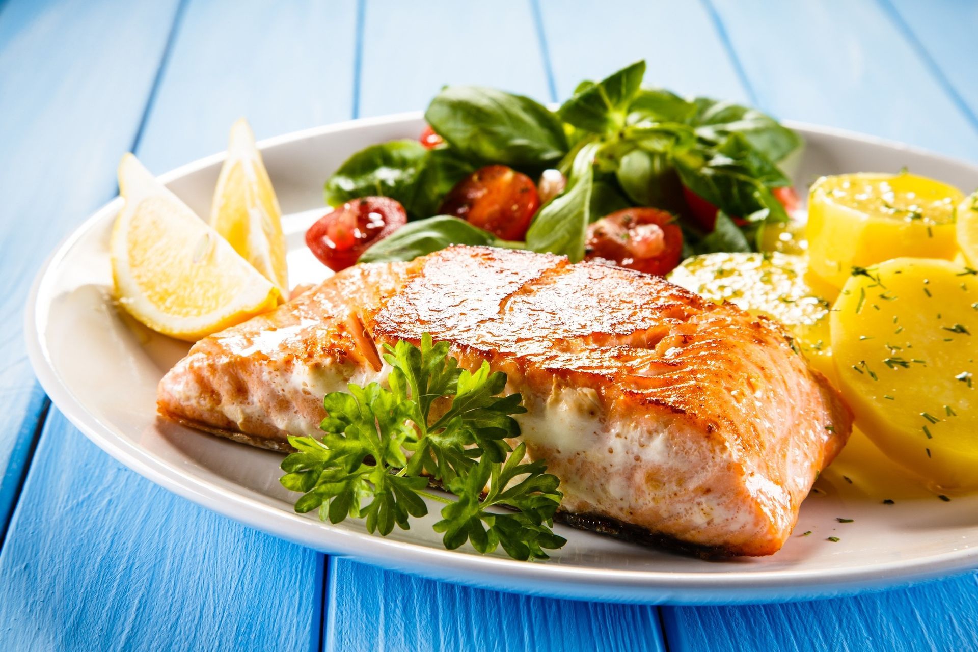 Grilled salmon with lemon, herbs, cherry tomatoes, and potatoes on a white plate