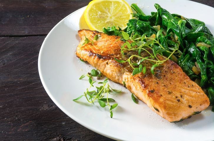 Grilled salmon on a white plate with sautéed greens and a lemon wedge