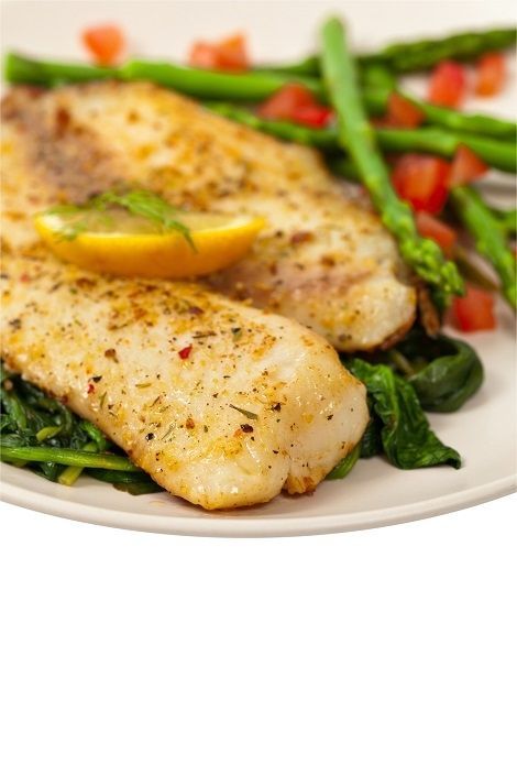 Seasoned fish fillets with lemon wedges and vegetables on a white plate
