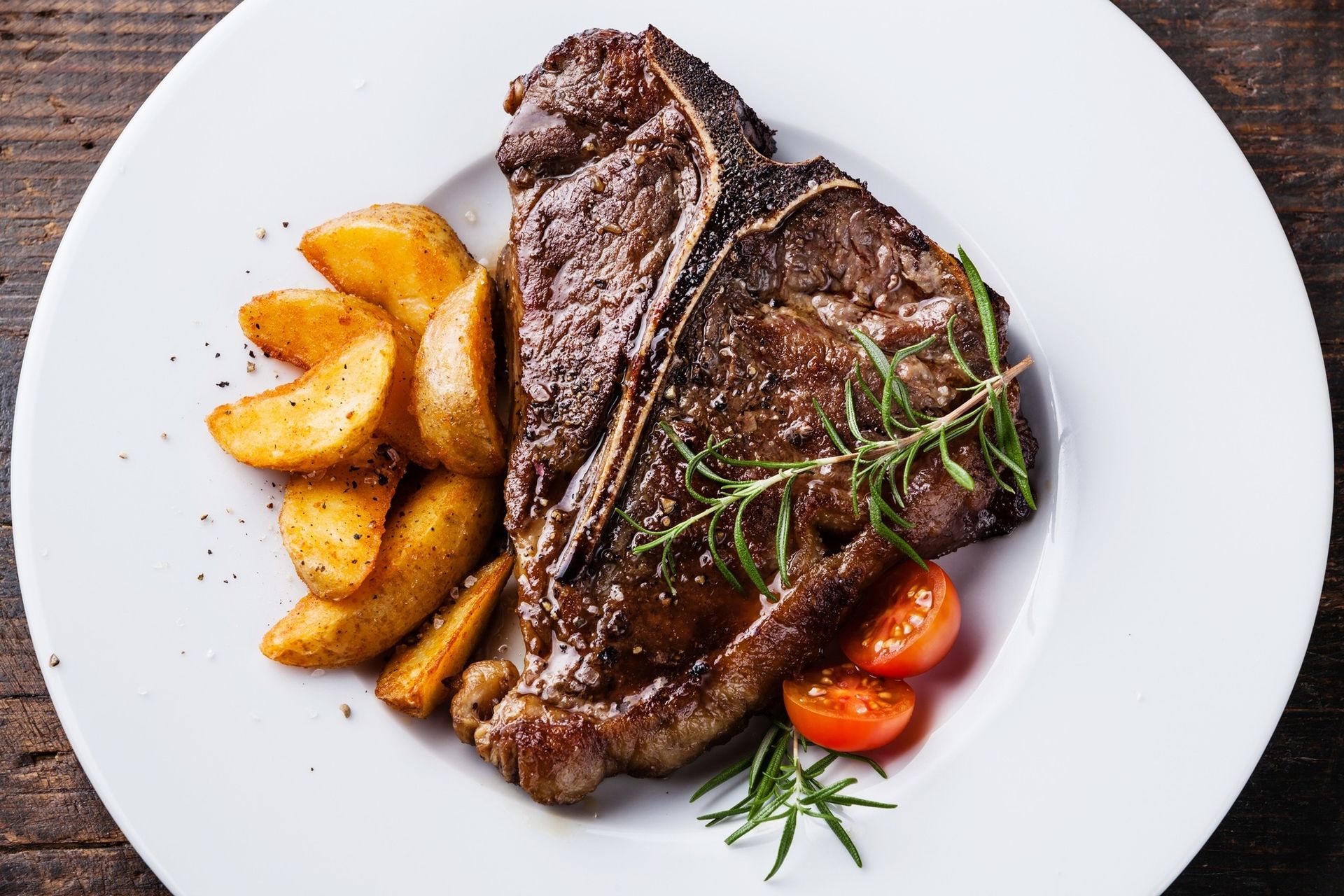 Grilled steak with roasted potato wedges and cherry tomatoes on a white plate