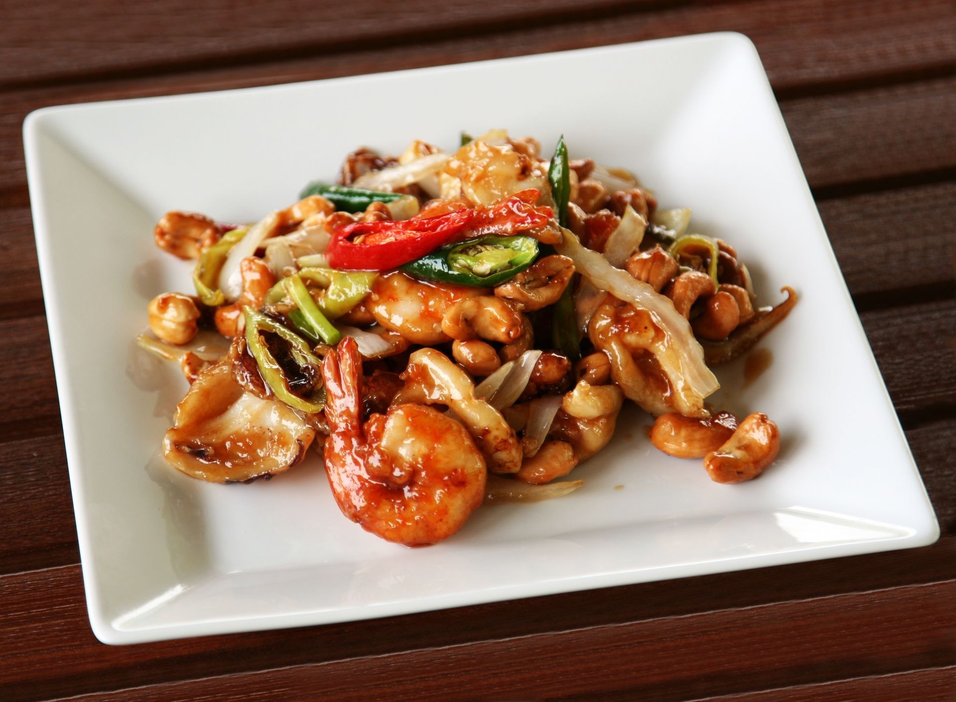 Stir-fried seafood and vegetables on a white square plate atop a wooden table