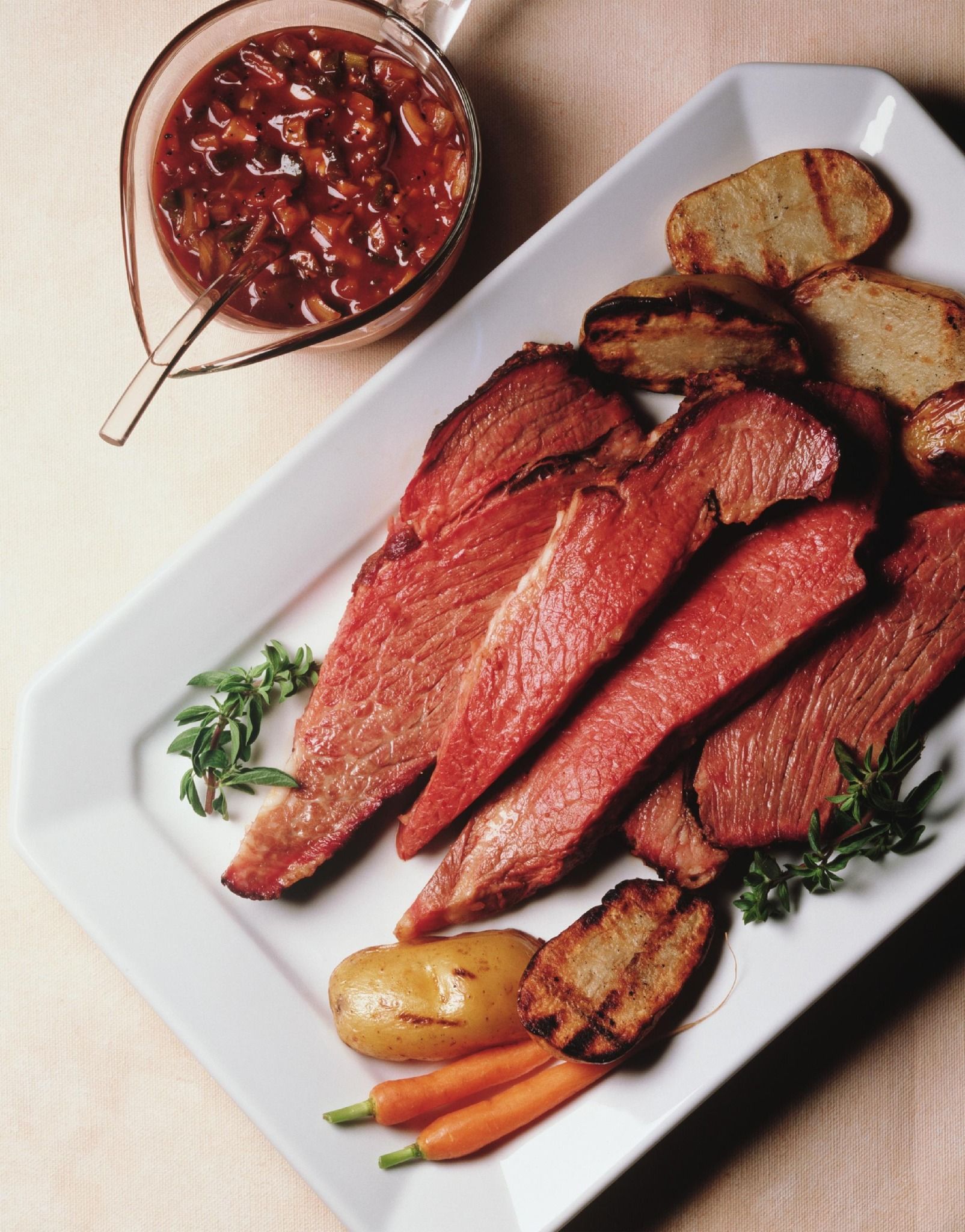 Sliced roasted meat on a platter with vegetables and a bowl of sauce