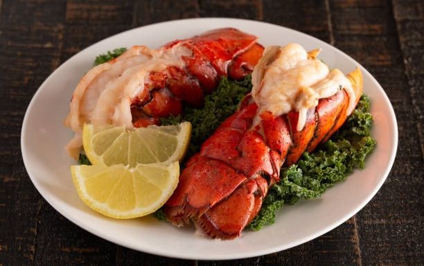Plated lobster tails with lemon wedges and greens on a white plate
