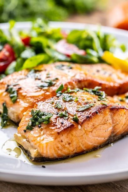 Grilled salmon fillet on a white plate with herbs and green salad