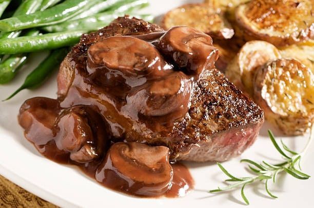 Steak topped with mushroom gravy, green beans, and roasted potatoes on a white plate