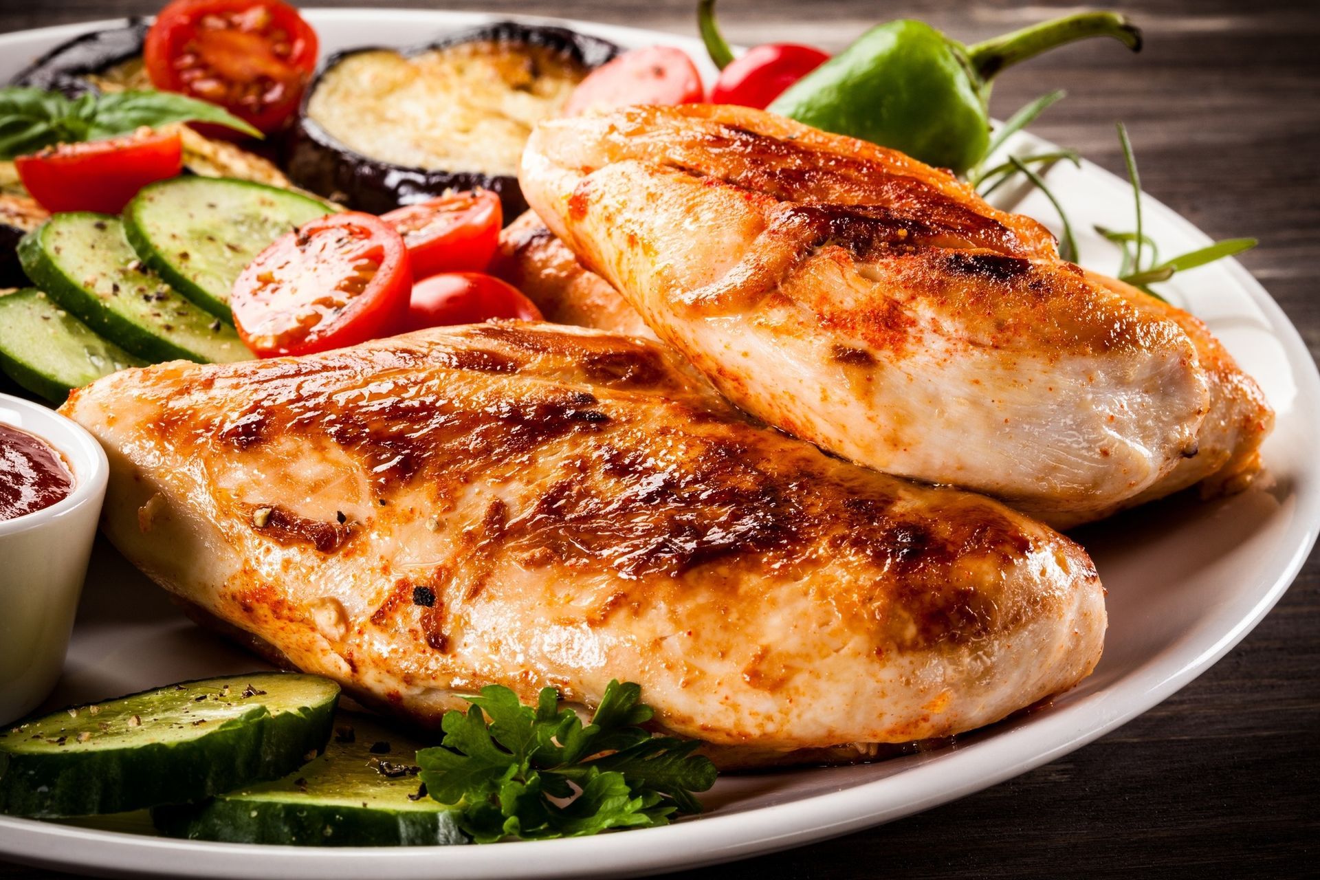 Grilled chicken breasts on a plate with cucumber, tomato, lime, and greens