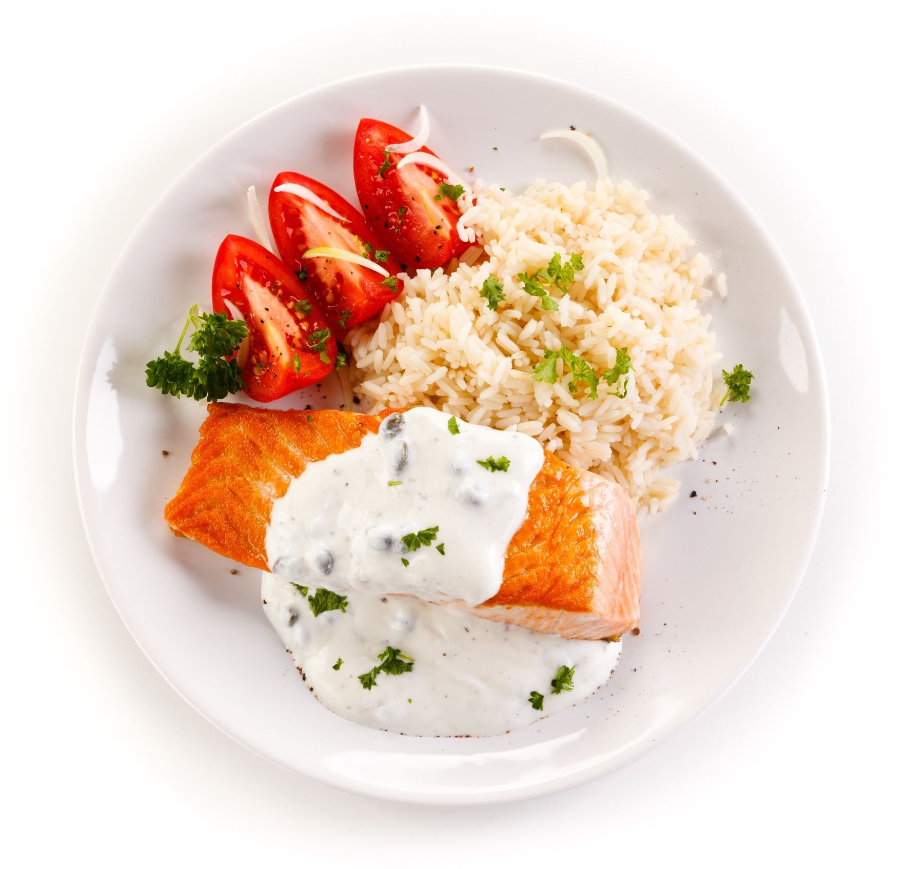 Salmon fillet with white sauce, rice, and sliced strawberries on a white plate
