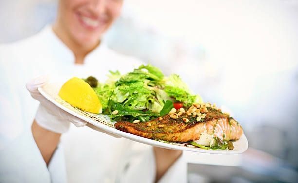 Waiter serving a plate of grilled fish with salad and lemon wedge
